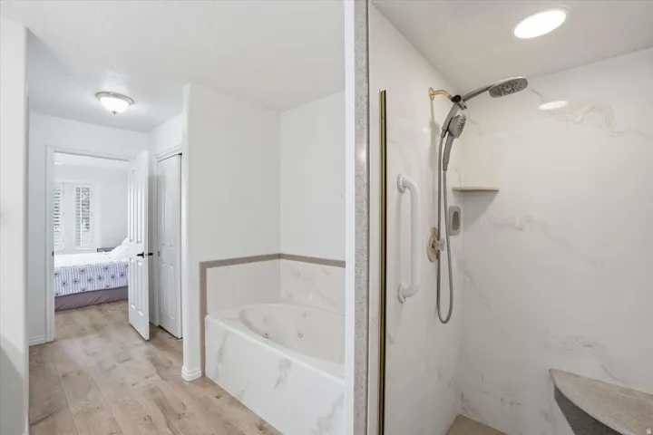 Jetted soaking tub with marble-look surround, walk-in shower with marble-look walls, built-in shower bench, and wood-finish flooring