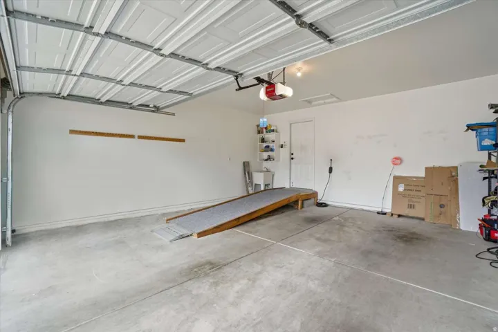 Concrete flooring, overhead garage door, built-in utility sink, and wall-mounted shelving