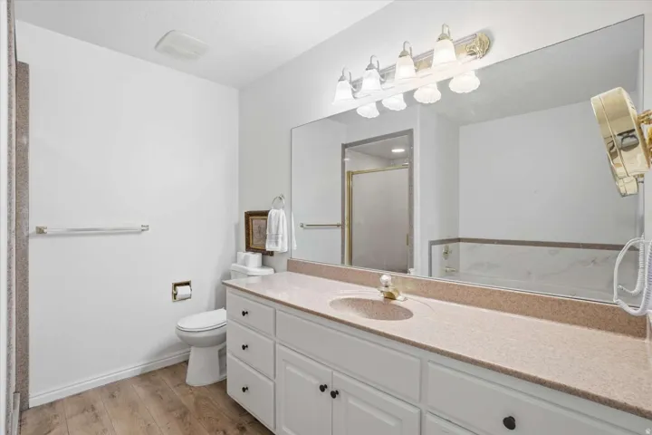 Vanity with single basin, stone-finish countertop, white cabinetry with dark hardware, and wood-finish flooring