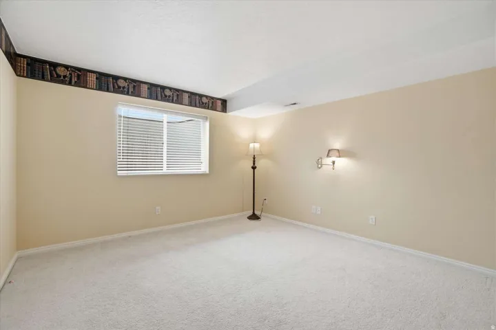 Expansive room featuring light-toned carpet flooring, light-colored walls, a window with horizontal blinds, and a decorative border