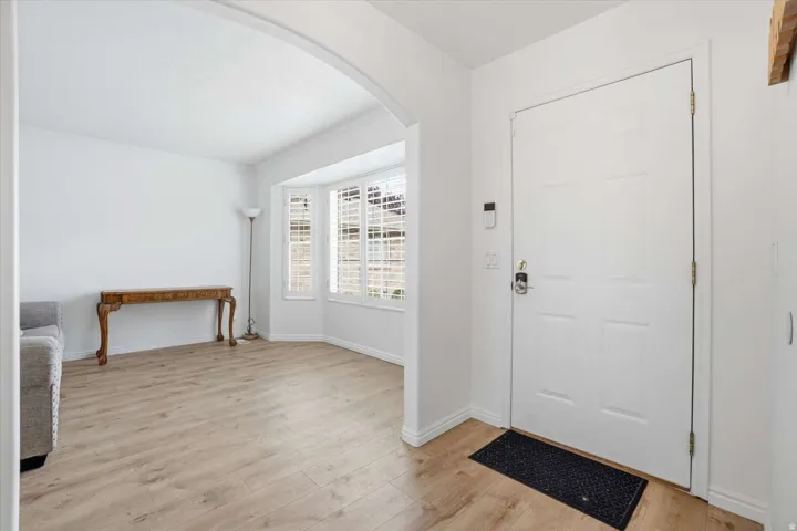 Entryway featuring a paneled door with modern hardware, wood-finish flooring, and an arched doorway opening to a living area with a bay window and plantation shutters