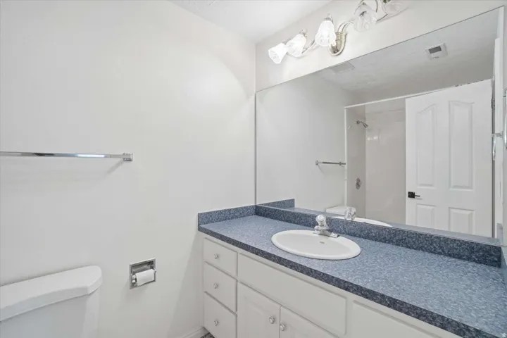 White vanity with lower cabinet storage, white oval basin sink, chrome faucet, and speckled blue countertop