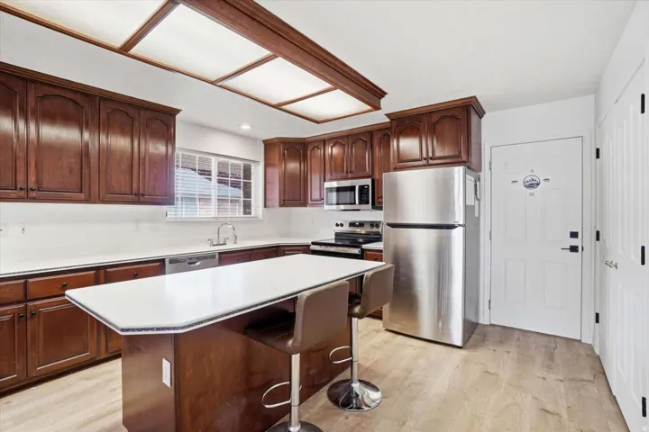 Kitchen featuring wood cabinetry, stainless steel appliances, white countertops, and wood-finish flooring