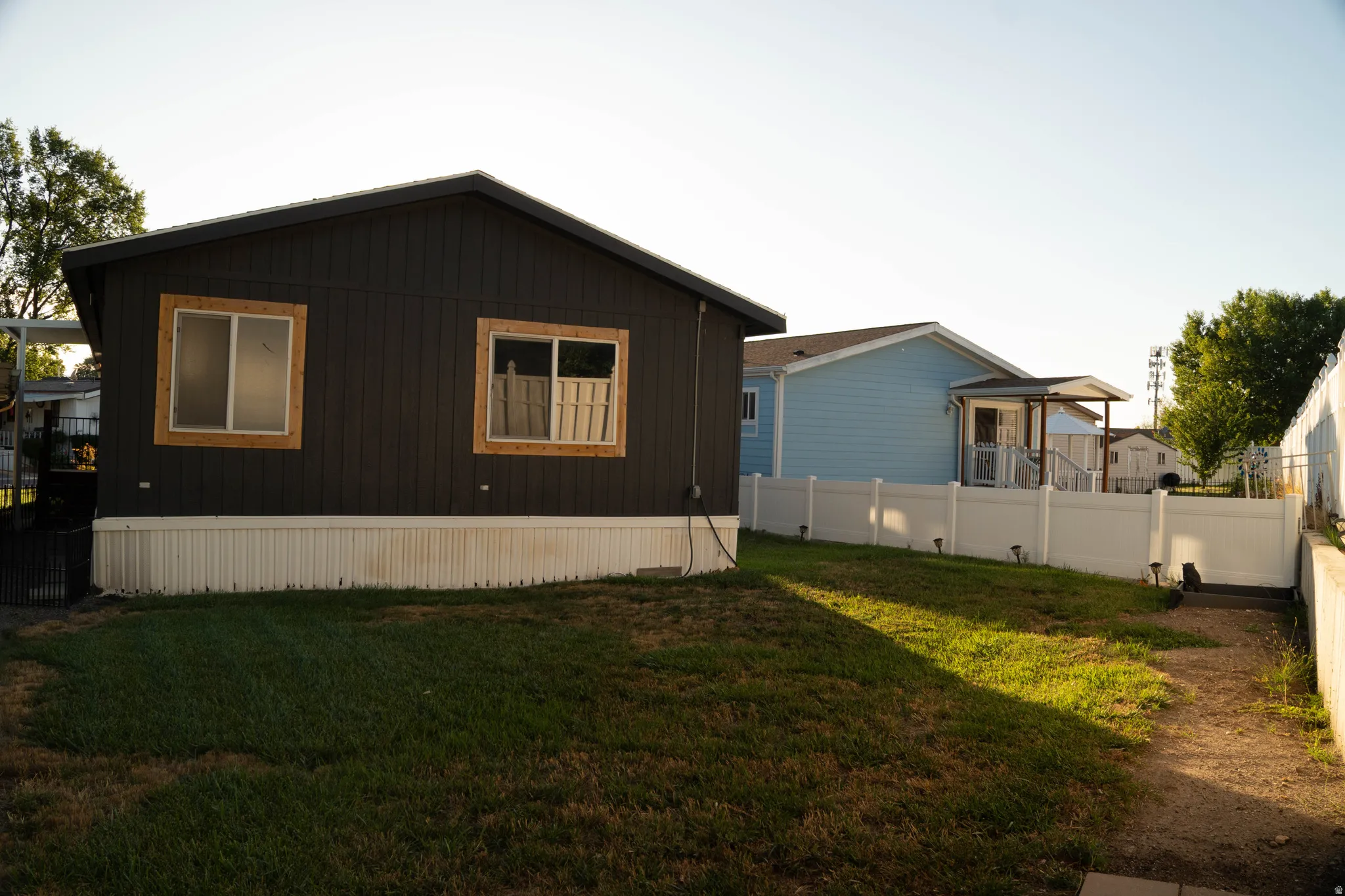 Dark-toned exterior siding with wood-framed windows, white vinyl fencing, and a gravel pathway
