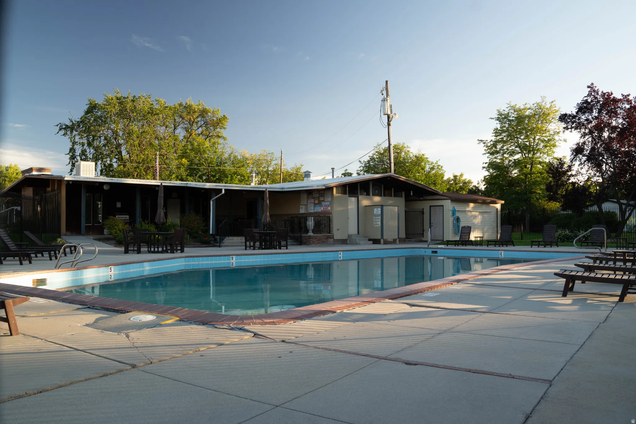 Expansive swimming pool with surrounding concrete deck, permanent pool house, and mature perimeter landscaping