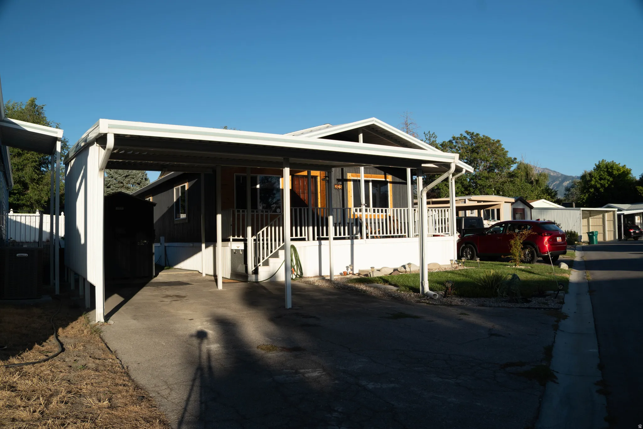 Covered carport, elevated front porch, exterior wood-finish siding, white railing, mountain backdrop
