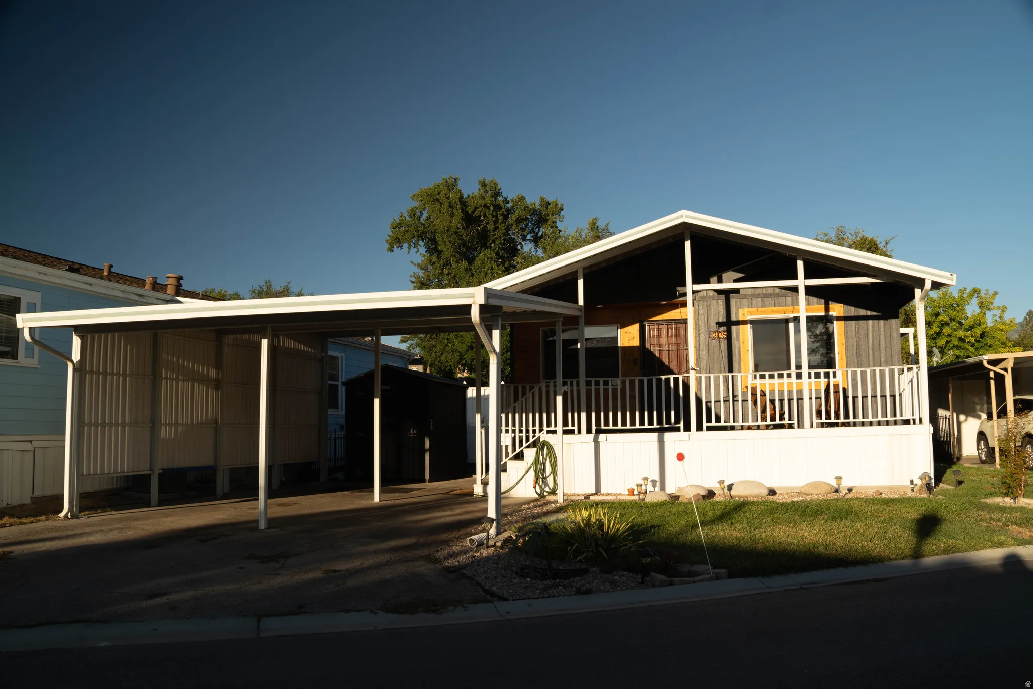 Carport with paved surface, covered porch with white railing, and exterior siding