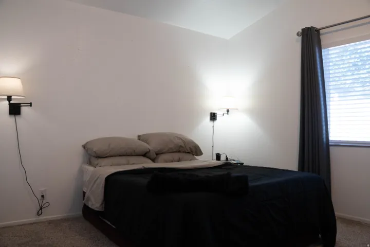 Wall-mounted sconce lighting, window with horizontal blinds, and carpeted flooring