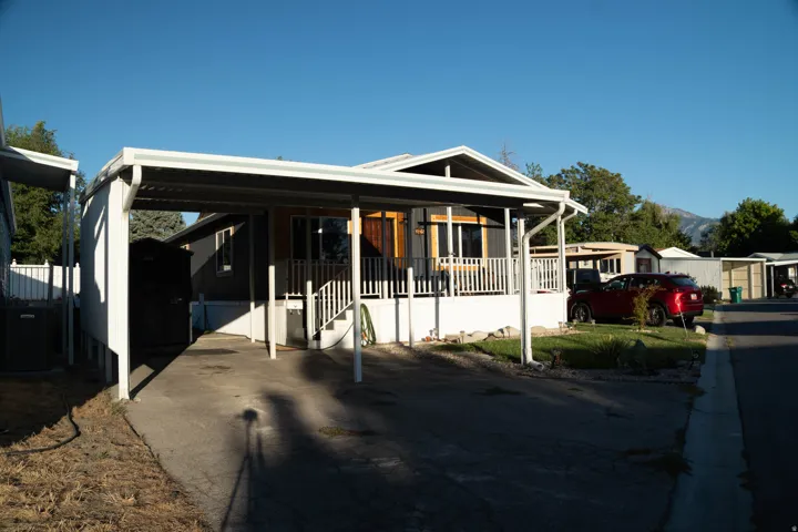 Covered carport, elevated front porch, exterior wood-finish siding, white railing, mountain backdrop