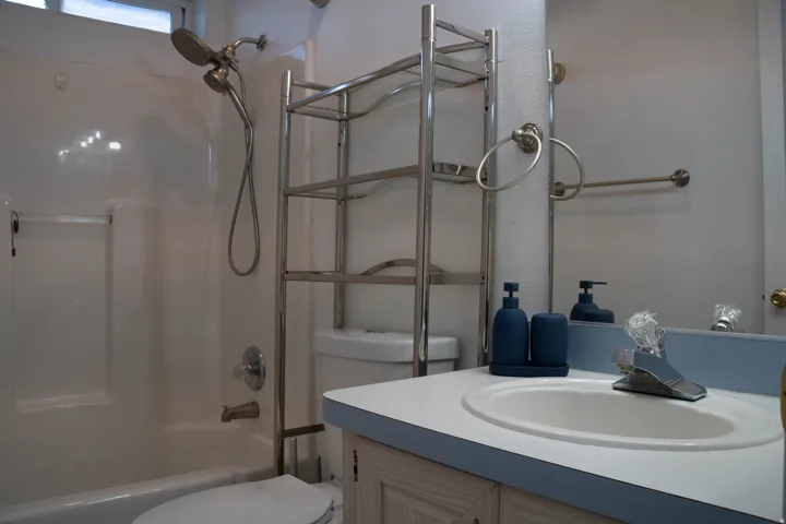 White integrated sink, chrome faucet, wood-finish vanity, and a full-width wall mirror