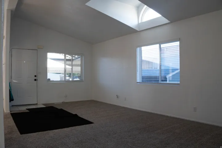 Vaulted ceiling with skylight, dual pane windows, and neutral carpet flooring