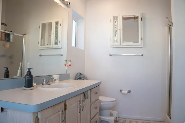 Vanity with integrated sink, chrome faucet, wall-mounted medicine cabinet, and glass-enclosed shower