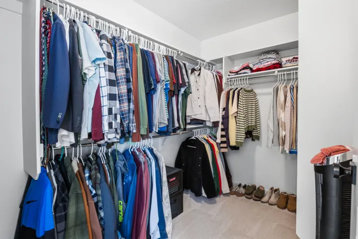 Walk-in closet with carpet flooring, white shelving, and multiple hanging rods for storage