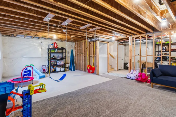Spacious unfinished basement offering exposed ceiling joists, framed partition walls, and partial rough-in plumbing