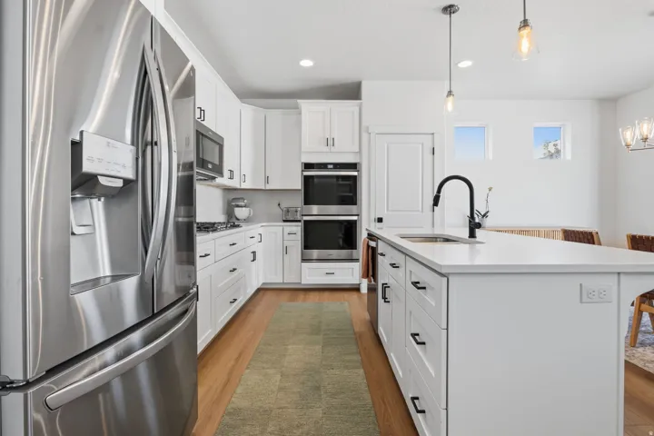 Kitchen featuring white cabinetry, stainless steel appliances, a center island with sink, pendant lighting, and wood-finish flooring