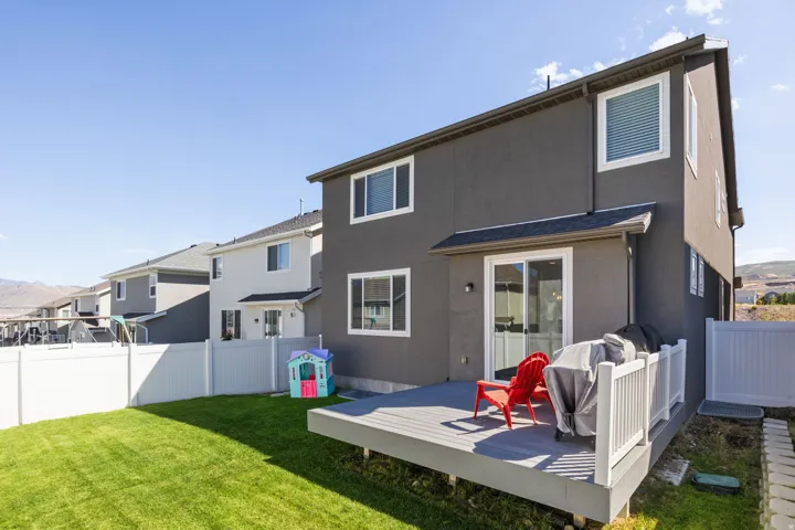 Expansive backyard featuring a manicured lawn, white vinyl fencing, and a dark gray composite deck