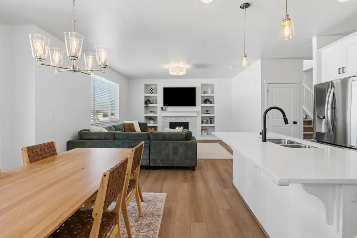 Open-concept living area with wood-finish flooring, a white kitchen island with an undermount sink, and stainless steel appliances