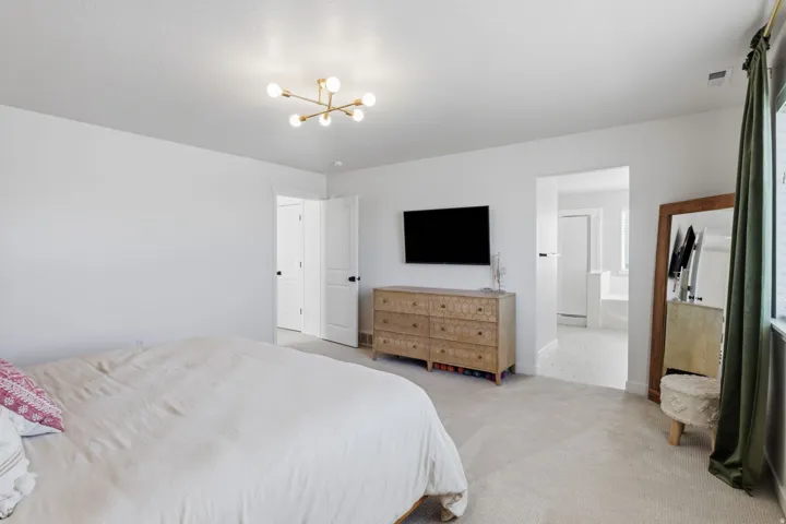 Recessed wall for media, contemporary light fixture, neutral carpet flooring, white interior doors, and an open doorway to a bathroom with a white tub