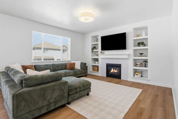 Wood-finish flooring, built-in shelving, fireplace with decorative surround, and a large window with blinds