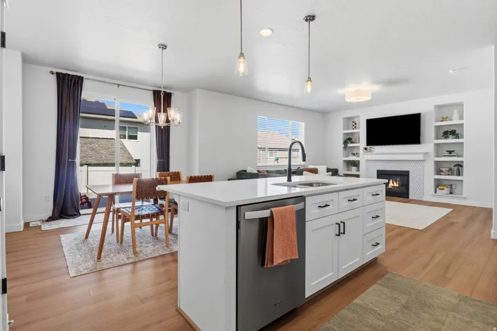 Open-concept living space with wood-finish flooring, a kitchen island featuring an integrated sink, and an electric fireplace with built-in shelving