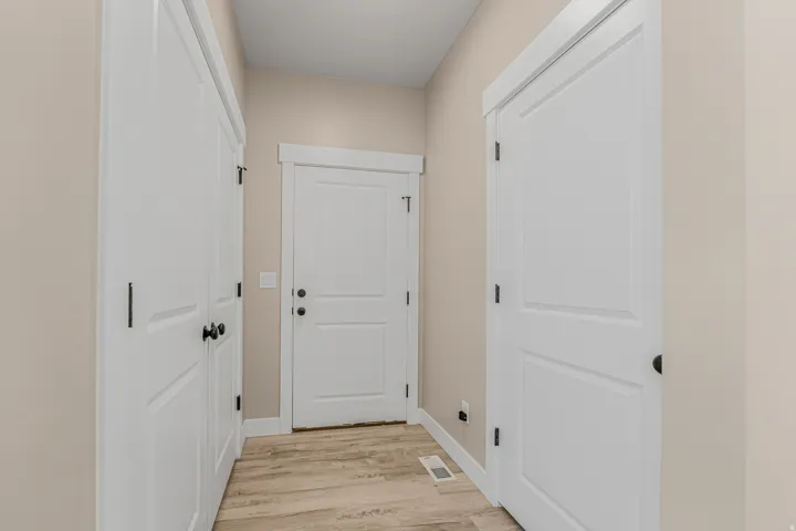 Interior hallway with wood-finish flooring, white paneled doors, and matte black hardware
