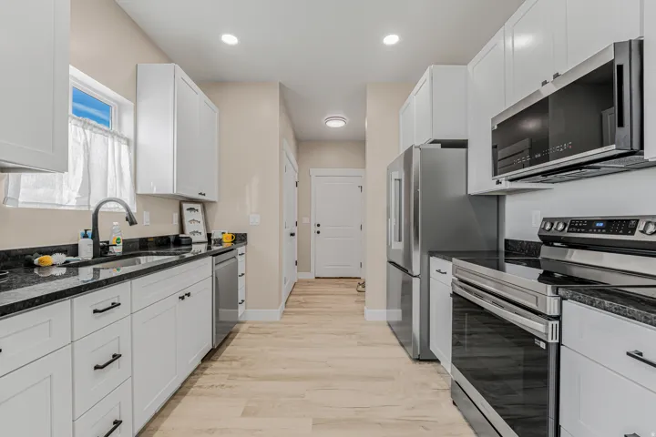 White cabinetry with black hardware, black countertops, stainless steel appliances, wood-finish flooring, and recessed lighting