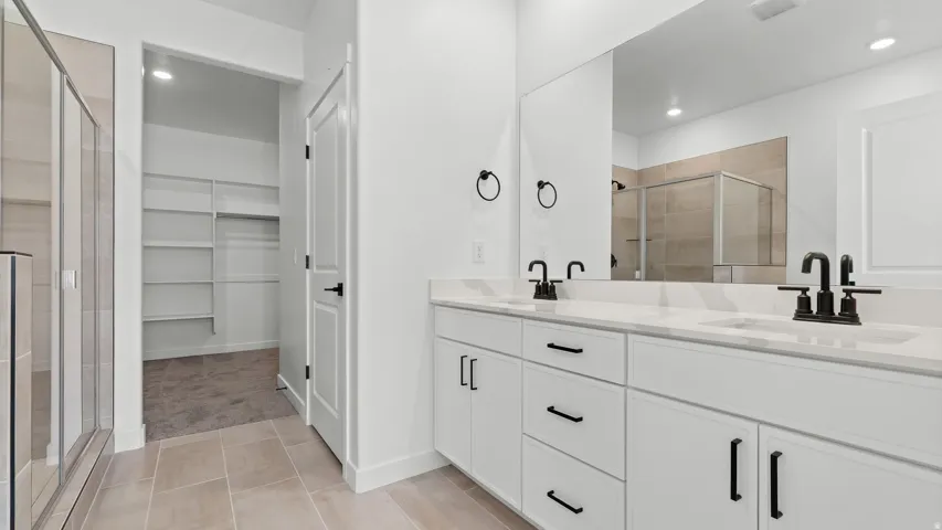 Dual vanity with white cabinetry and black hardware, stone-finish countertops, large mirror, and a glass-enclosed shower