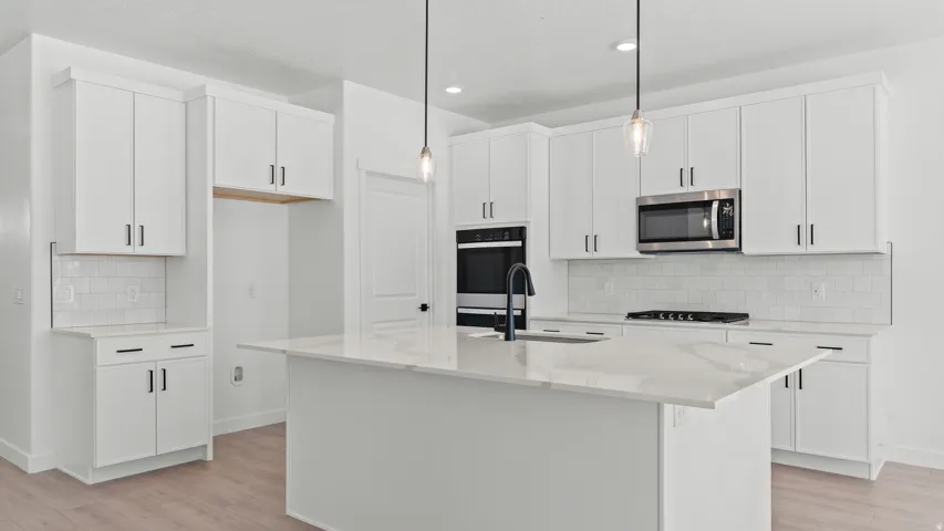 Modern kitchen featuring white cabinetry, a large center island with a stone-finish countertop, built-in stainless steel appliances, and a tiled backsplash