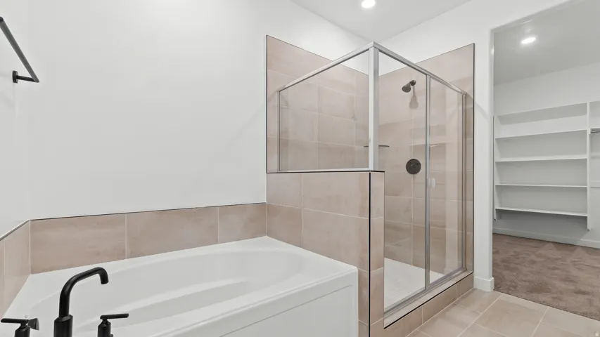 Soaking tub with matte black fixtures, glass-enclosed shower, and built-in shelving