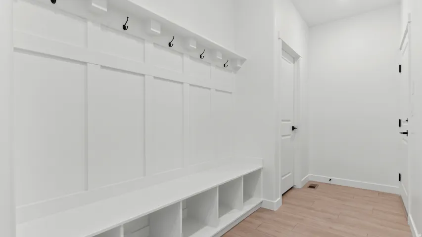 Built-in bench seating with cubbies and coat hooks, wood-finish flooring, white paneling, and white doors with matte black hardware