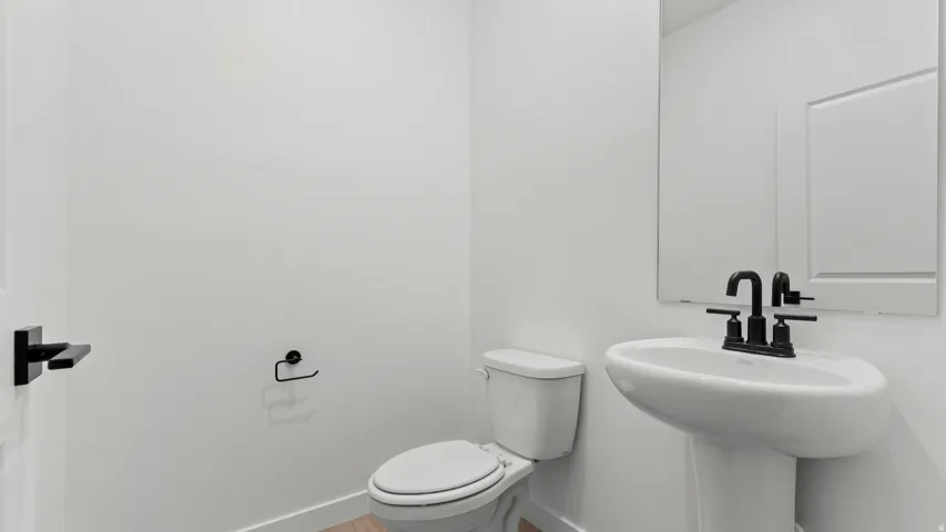 Pedestal sink with a matte black faucet, wall-mounted mirror, and wood-finish flooring