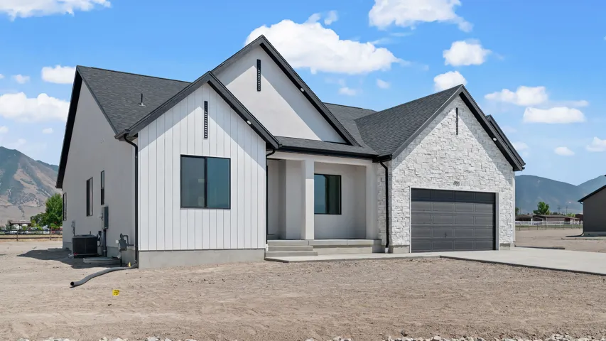 Modern exterior with a dark-pitched roof, white vertical siding, light-toned stone accents, a two-car garage, and a concrete driveway
