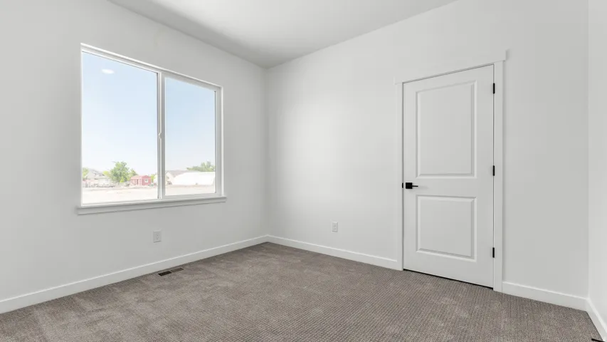 Bright room featuring soft gray carpeting, white walls, a white two-panel door with matte black hardware, and a large window