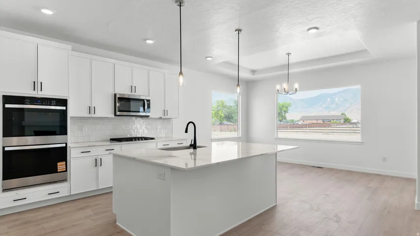 Kitchen featuring a large island with sink, white shaker-style cabinetry, stainless steel double ovens and microwave, and wood-finish flooring