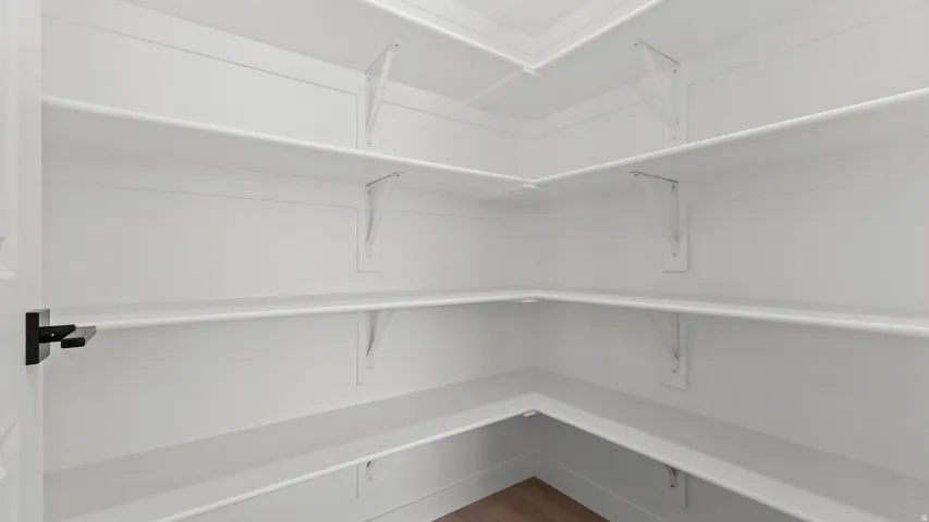 Walk-in pantry featuring white shelving, wood-finish flooring, and a black lever door handle