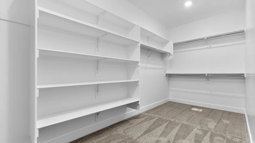 Integrated white shelving, multiple hanging rods, recessed ceiling lighting, and carpeted flooring