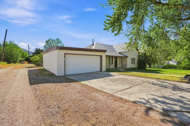Attached garage with white panel door, concrete driveway, and a front lawn with mature trees