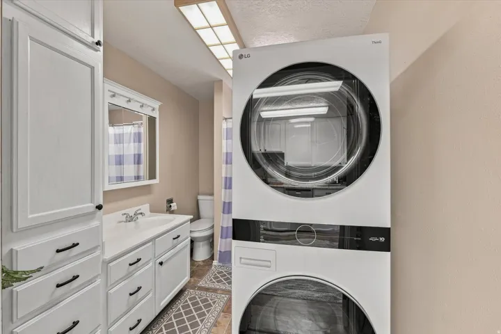 White shaker-style cabinetry with dark hardware, integrated vanity sink, mirrored medicine cabinet, and patterned floor tiling