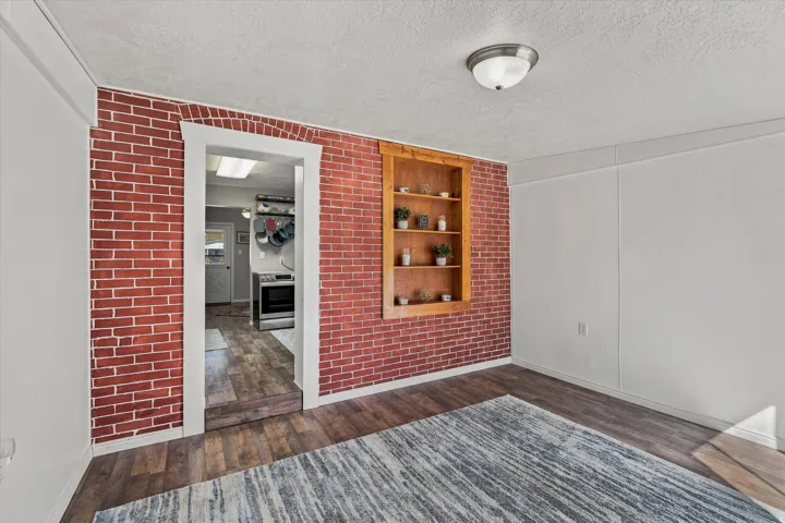Exposed brick accent wall, wood-finish flooring, built-in shelving, white trim, and a flush mount ceiling light