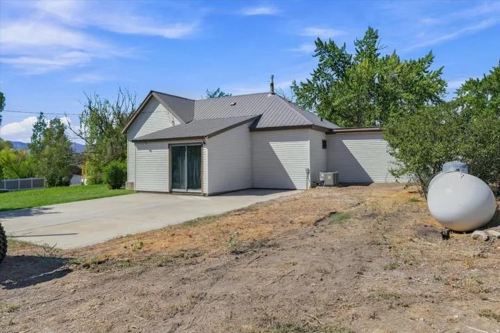 Metal roof, light-toned siding, sliding glass door, concrete patio, air conditioning unit
