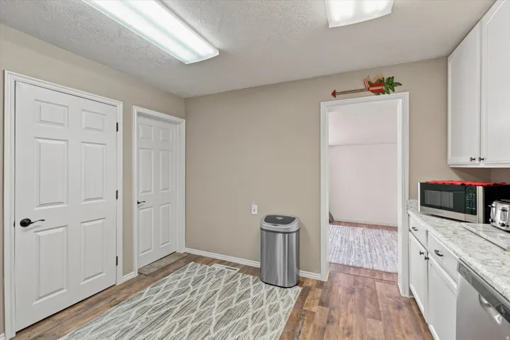 Wood-finish flooring, white panel doors, overhead fluorescent lighting, and white cabinetry with dark hardware