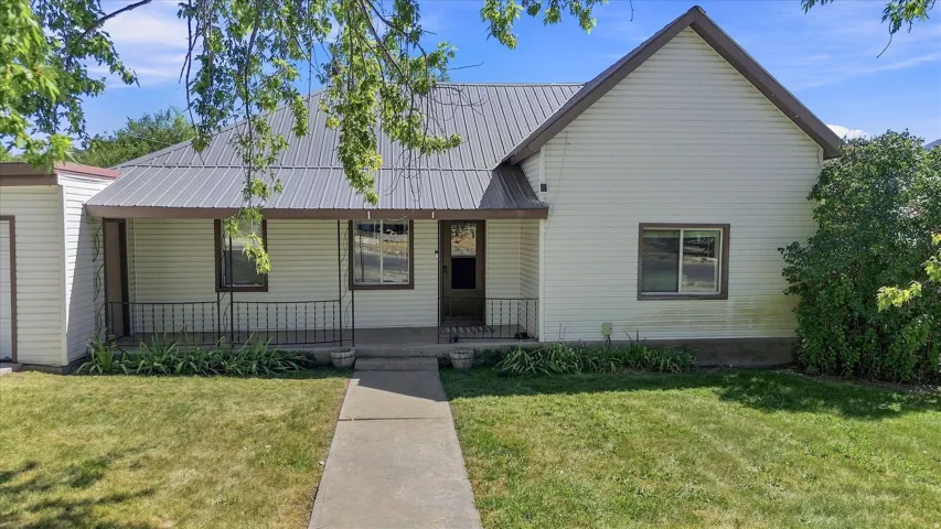 Metal roof, covered front porch with railings, white siding, attached single-car garage, and established front lawn