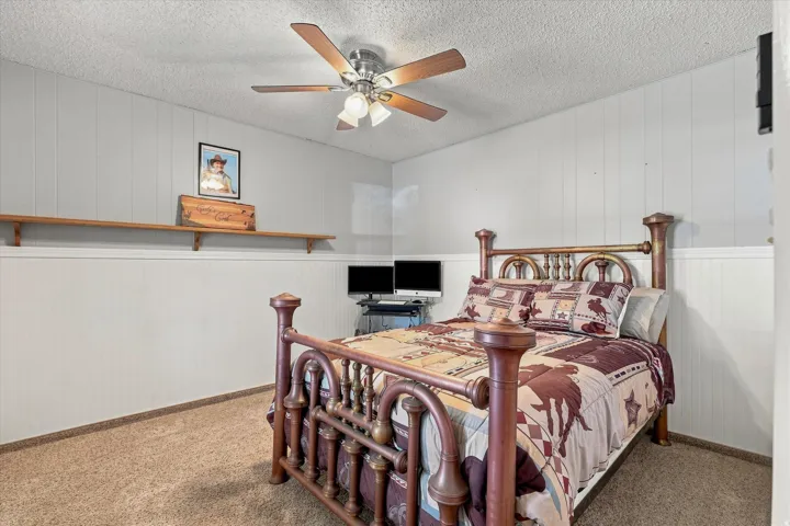 Wall paneling with wood shelving, ceiling fan with integrated lighting, and carpeted flooring