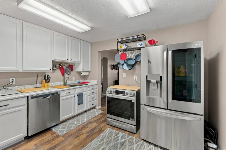 White cabinetry with black hardware, stainless steel appliances, wood-finish flooring, light-toned countertops, and recessed lighting