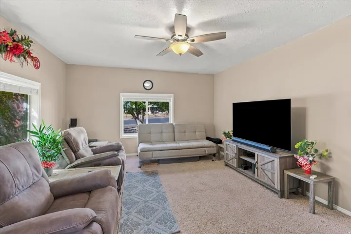Living area featuring neutral wall tones, carpeted flooring, multiple windows, and a ceiling fan with integrated lighting
