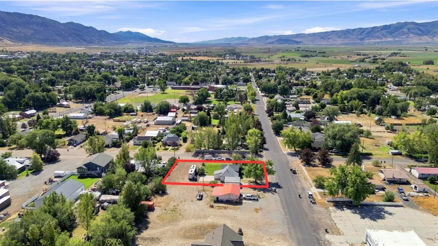 Aerial perspective showcasing the property's location within a developed area, featuring an asphalt street, surrounding residential structures, and distant mountains