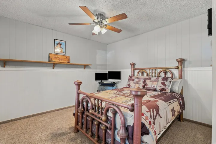 Textured ceiling, ceiling fan with integrated lighting, wall paneling, and wall-mounted shelving
