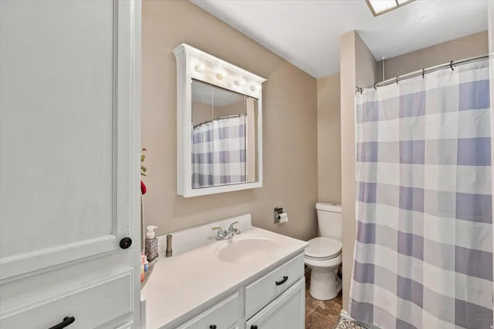 White vanity with integrated sink, wall-mounted mirror with overhead lighting, and built-in storage cabinetry
