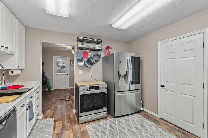 Kitchen featuring stainless steel appliances, white cabinetry, wood-finish flooring, and white countertops