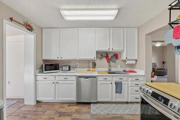Kitchen featuring white cabinetry, light-toned countertops, a stainless steel dishwasher, and wood-finish flooring